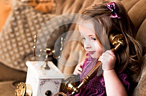 Charming little girl with a purple bow on her head calls on a retro telephone