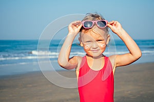 Charming little girl puts on sunglasses on the beach