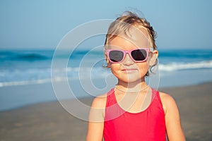 Charming little girl puts on sunglasses on the beach