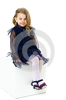 Charming little girl sitting on white cube studio