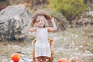 Charming little girl in a straw hat, wicker chair, pumpkins