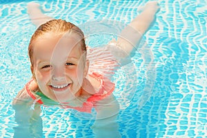 Charming little girl swims in the pool. The child is smiling and looking at the camera