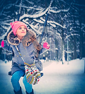 Charming little girl on swing in snowy winter