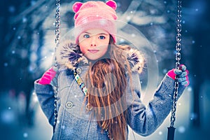 Charming little girl on swing in snowy winter