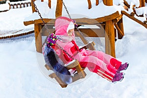 Charming little girl on swing in snowy winter