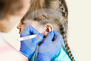 A charming little girl is undergoing the procedure of ear piercing by a professional medical worker. Adorable little girl having