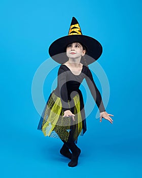 charming little girl in a witch costume dancing in the studio on a blue background