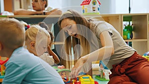 charming long-haired Caucasian teacher playing with her beloved kids at the nursery, medium shot