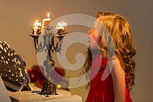 Charming long-haired girl sits at the piano and blows out the candle.