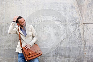 Charming man with leather bag standing against wall