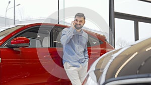 Charming man talking on his smart phone while choosing new car at the dealership