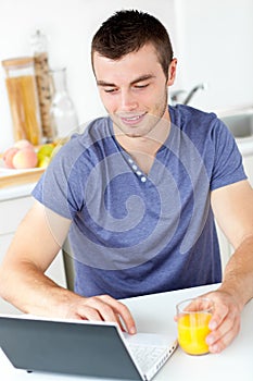 Charming man using his laptop holding orange juice