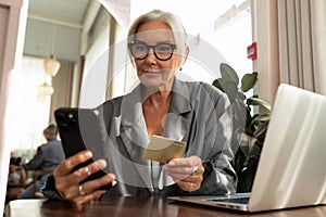 charming mature business woman pays for the order online using a smartphone while sitting in a cafe