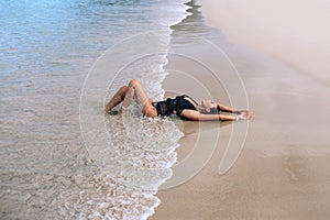 Charming miss in a stylish black swimsuit and bright makeup lies and relaxes on the beach.