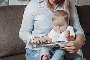 Charming mother showing images in a book to her cute little son at home sitting on the couch