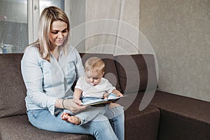 Charming mother showing images in a book to her cute little son at home sitting on the couch