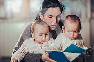 Charming mother showing images in a book to her cute twin babies