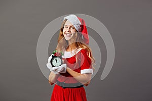 Charming mrs.Santa Claus dressed in the red robe, Santa`s hat and white gloves is holding a clock that shows five to