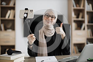 Charming muslim woman in hijab talking and gesturing while recording video on modern phone on stick