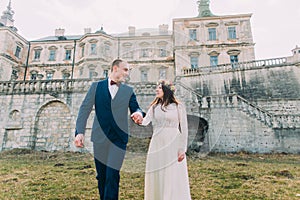 Charming newlywed bride and groom walking near beautiful ruined baroque palace