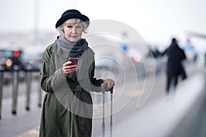 Charming old woman is posing pensively with smartphone