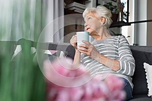 Charming old woman relaxing on couch with hot drink