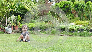 Charming one year old baby boy learning to stand and sit on his own on the grass.