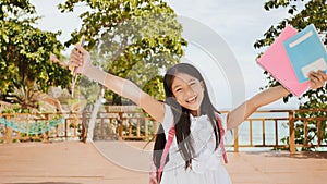 A charming philippine schoolgirl with a backpack and books in a park off the coast. A girl joyfully poses, raising her