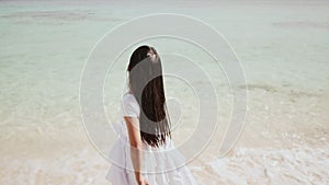 A charming philippine schoolgirl in a white dress is walking along a white sandy beach. Enjoying the tropical scenery