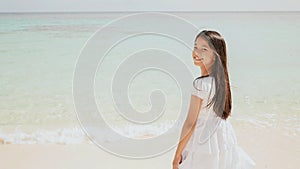 A charming philippine schoolgirl in a white dress is walking along a white sandy beach. Enjoying the tropical scenery