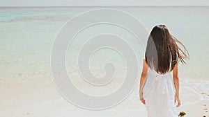 A charming philippine schoolgirl in a white dress is walking along a white sandy beach. Enjoying the tropical scenery