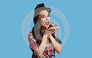 Charming pinup lady in retro wear eating chocolate cake on blue studio background
