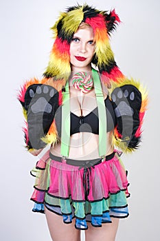 Charming plus size young woman in fur hat made of multicolored fibers with cat ears and paws posing in green suspenders, black bra