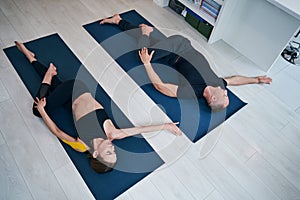 Charming pretty woman and neat male practicing supine twist yoga pose in modern studio