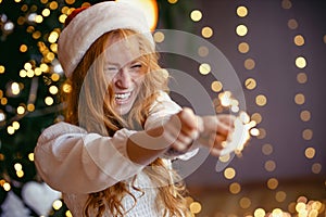 charming red-haired girl in a santa hat with sparklers in her hands smiling at the camera