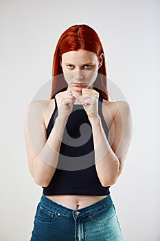 Charming redhead long-haired girl dressed in black top and jeans keeps hands in fists on the white background in the