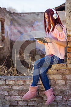 Charming Redhead Woman Enjoying Music on Tablet in Sunset Ruins