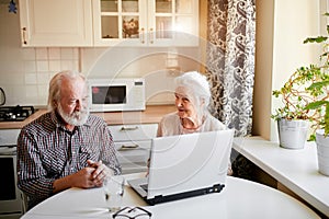 Charming senior couple using laptop sitting at the table in the kitchen room.