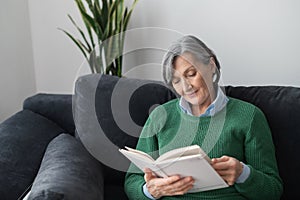 Charming senior lady reading a book on the sofa