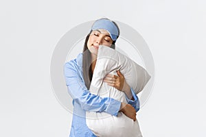 Charming sleeping asian girl in eyemask and pyjama, hugging pillow and lying on it with closed eyes, dreaming, having