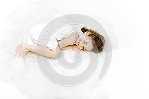 Charming sleeping little girl angel on soft white fur, isolated on white background.