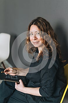 Charming smiling adult woman middle aged woman with curly hair architect designer with drawing plan in hands in the modern office