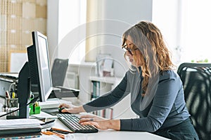 Charming smiling adult woman middle aged woman with curly hair architect designer working on computer in bright modern office