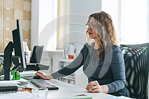 Charming smiling adult woman middle aged woman with curly hair architect designer working on computer in the bright modern office