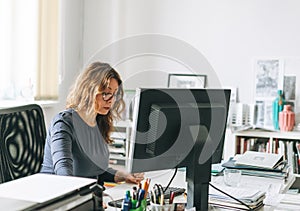 Charming smiling adult woman middle aged woman with curly hair architect designer working on computer in the bright modern office