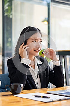 Charming and smiling Asian female customer service worker wearing headset in online meeting office look at laptop computer screen,