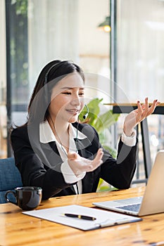 Charming and smiling Asian female customer service worker wearing headset in online meeting office look at laptop computer screen,