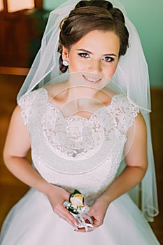 Charming smiling bride with stylish make-up in white dress posing, holding cute little boutenniere