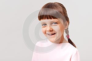 Charming smiling female child wearing pink sweater looking at camera with happy expression, brown haired having positive emotions