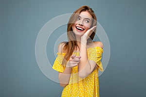 Charming smiling good looking young blonde woman wearing stylish yellow summer dress standing  over blue